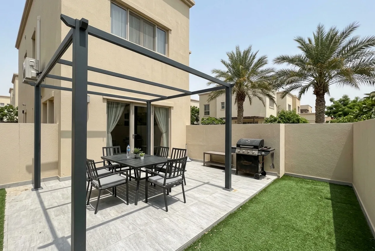 A clean villa patio in Dubai with a dark pergola over light grey tiles, an outdoor dining table, a barbecue and artificial grass