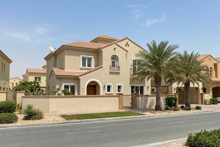 A two-storey Spanish-style villa with beige walls, a terracotta tile roof and palm trees on a quiet street in The Villa, Dubailand