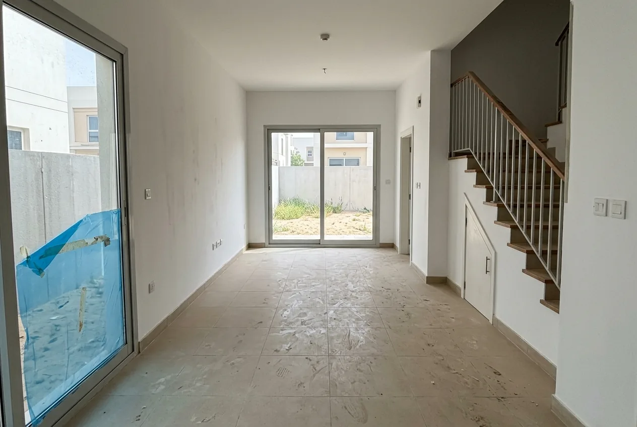 An empty new townhouse in Villanova on handover day, with construction dust on the floor tiles and protective film still on the sliding door
